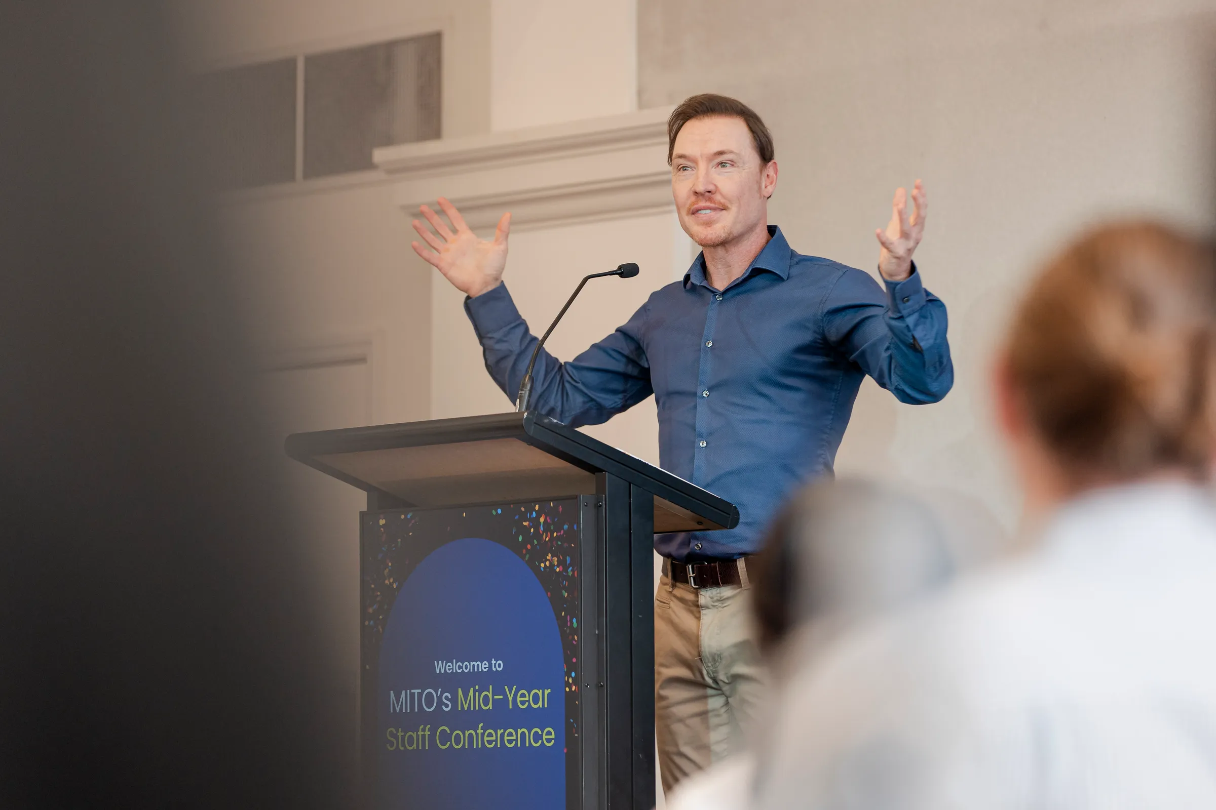 Bradley Hook keynoting at a staff conference, arms open at the lectern